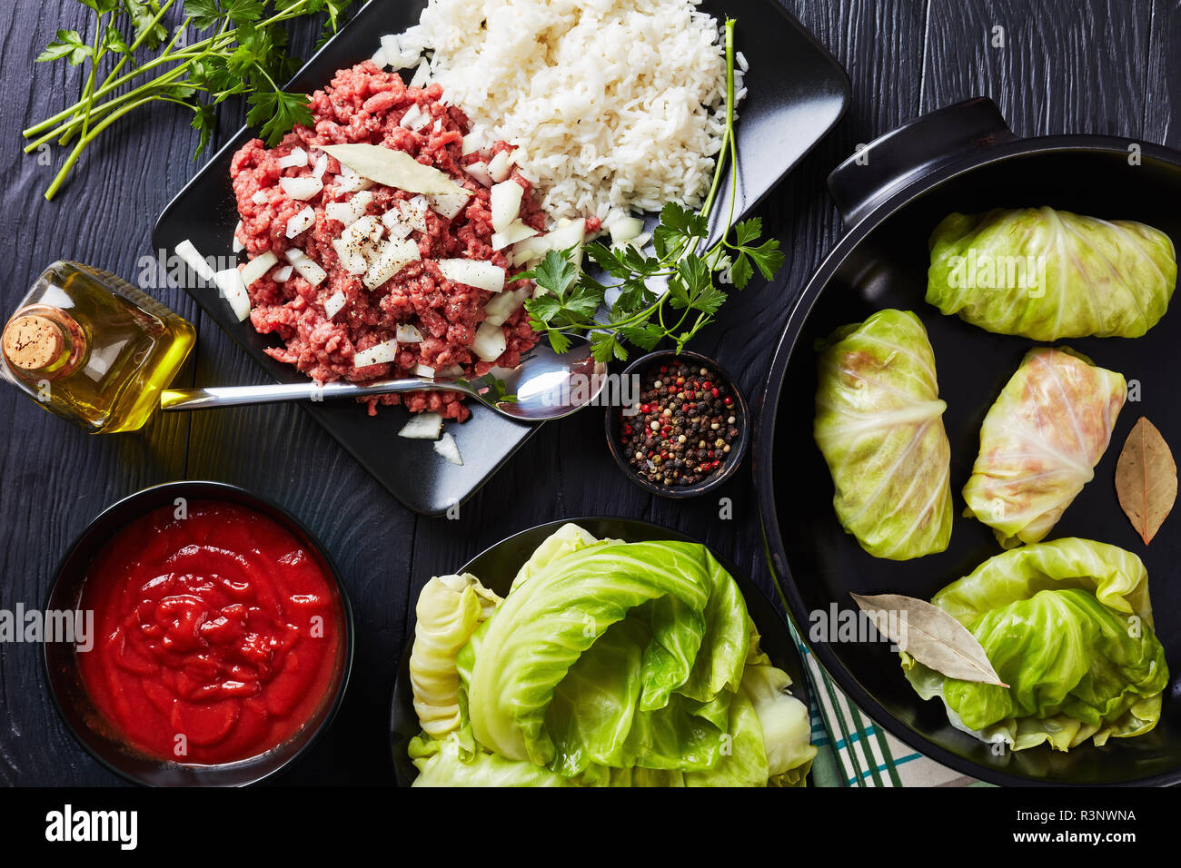 Feuilles de chou farcies non cuites avec des ingrédients - la viande hachée, le riz cuit, le persil et la sauce tomate sur un tableau noir, vue de dessus, flatlay Banque D'Images