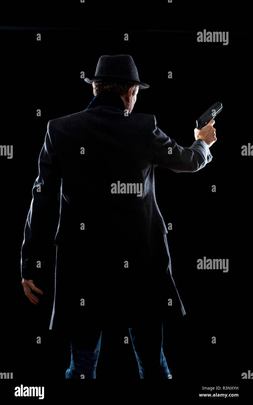 Silhouette d'un homme avec une arme portant un manteau et trilby Banque D'Images