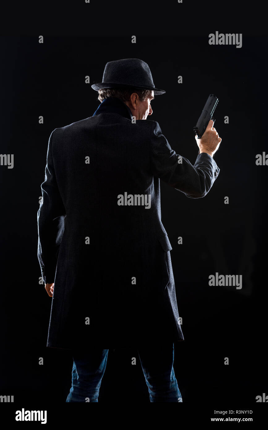 Silhouette d'un homme avec une arme portant un manteau et trilby Banque D'Images