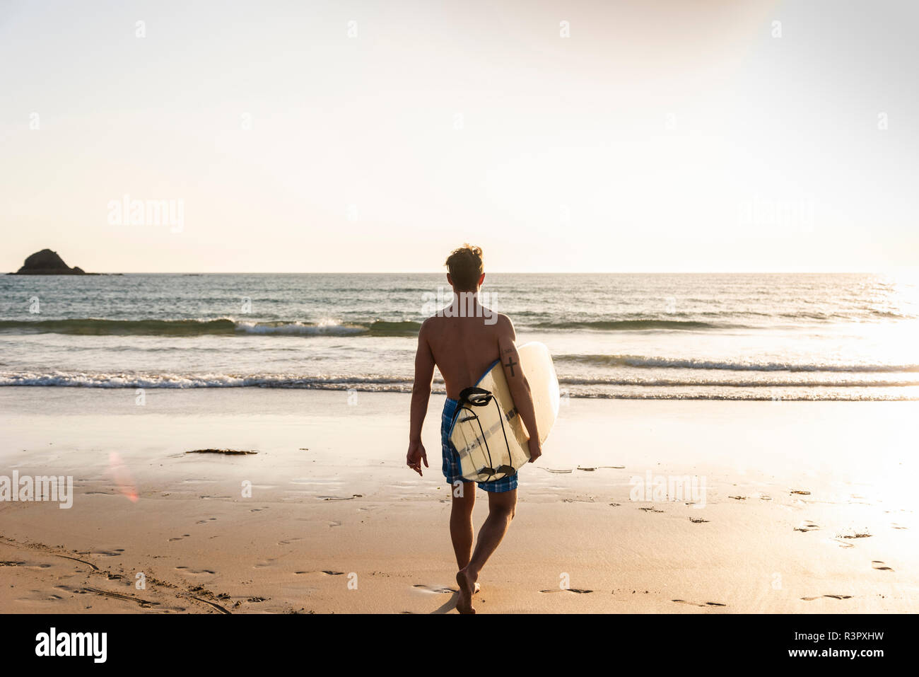 Jeune homme marchant sur la plage, sa planche de surf Banque D'Images