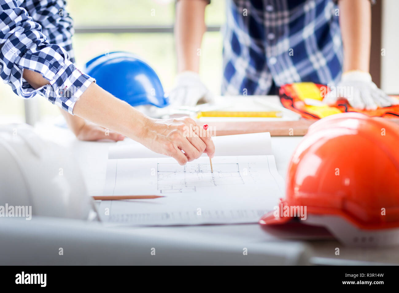 La main libre de l'ingénieur manager signaler avec red pin point sur construction blueprint sur la table de travail en chantier avec casque de sécurité en pl Banque D'Images