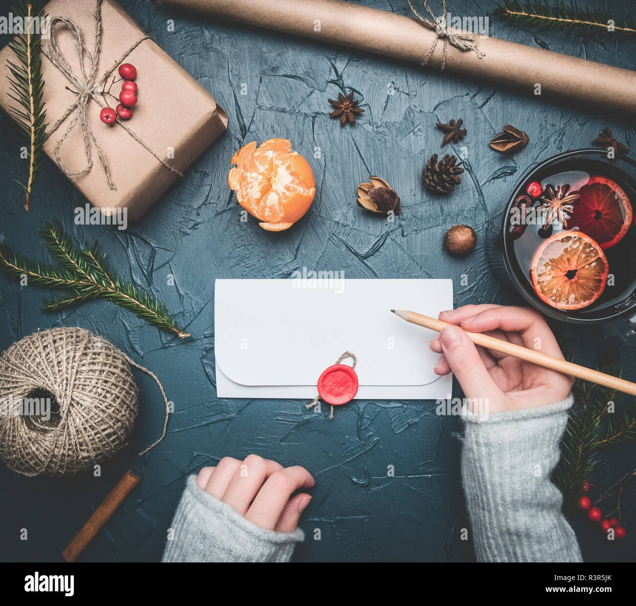 Fille signe une enveloppe avec félicitations pour la nouvelle année ou de Noël, à côté se trouve un cadeau, tangerines, matériaux d'emballage, tasse de vin chaud, mandari Banque D'Images