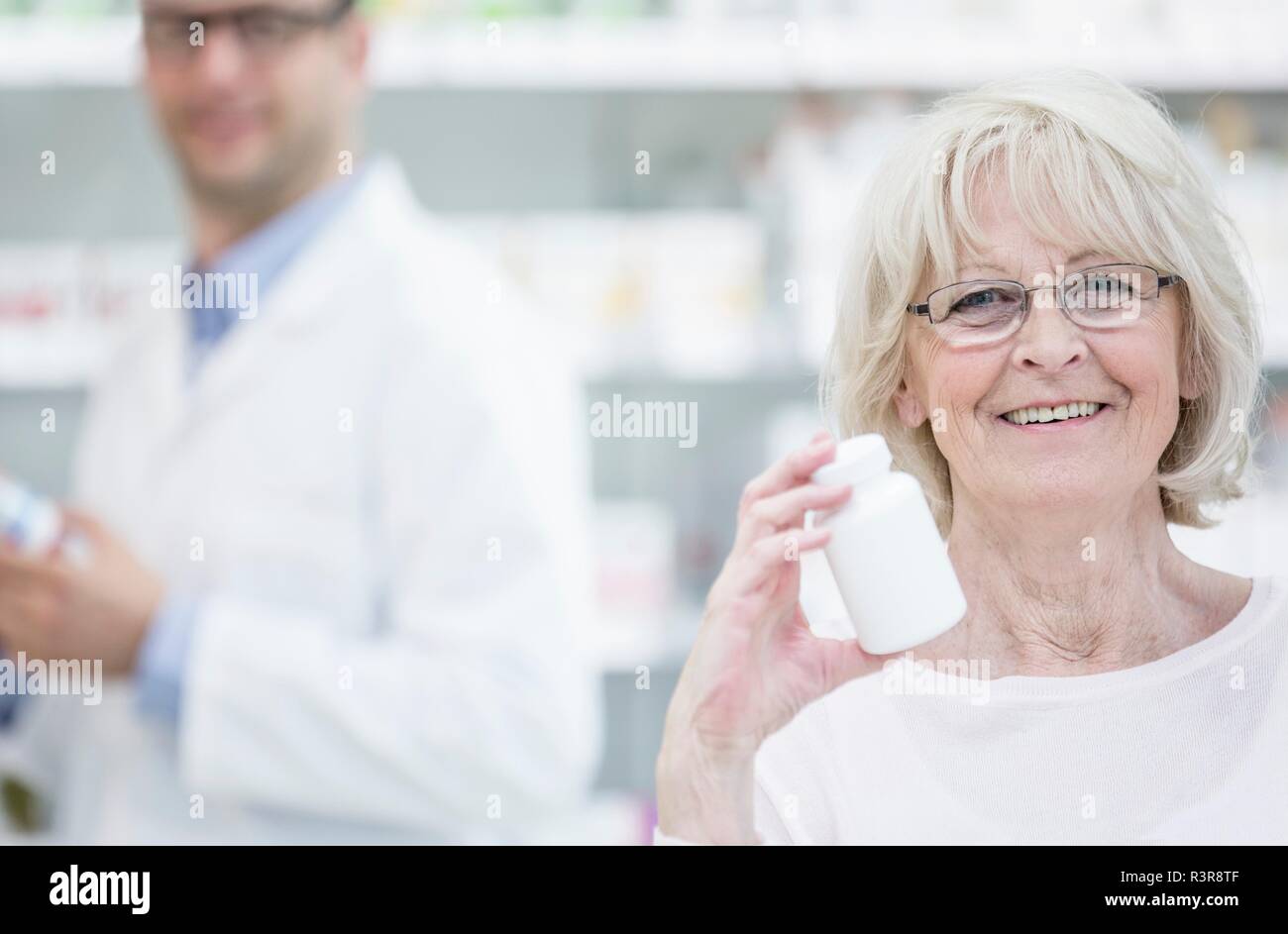 Portrait of senior woman holding bouteille de pilules en pharmacie, pharmacien avec en arrière-plan. Banque D'Images