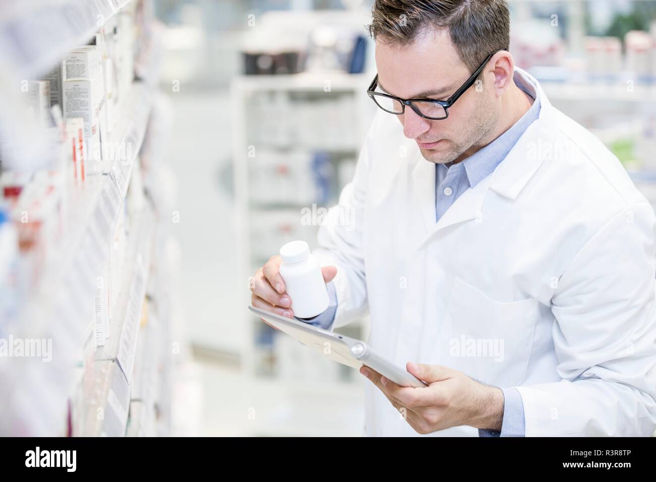 Pharmacien mâle using digital tablet pour vérifier bouteille de pilules en pharmacie. Banque D'Images