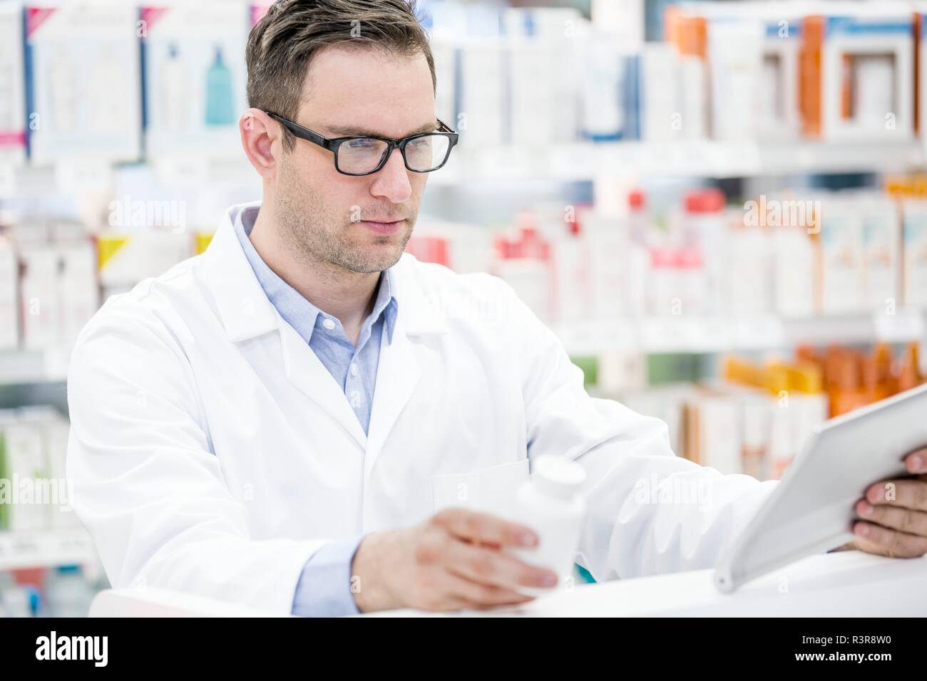 Jeune homme pharmacien using digital tablet pour vérifier bouteille de pilules en pharmacie. Banque D'Images