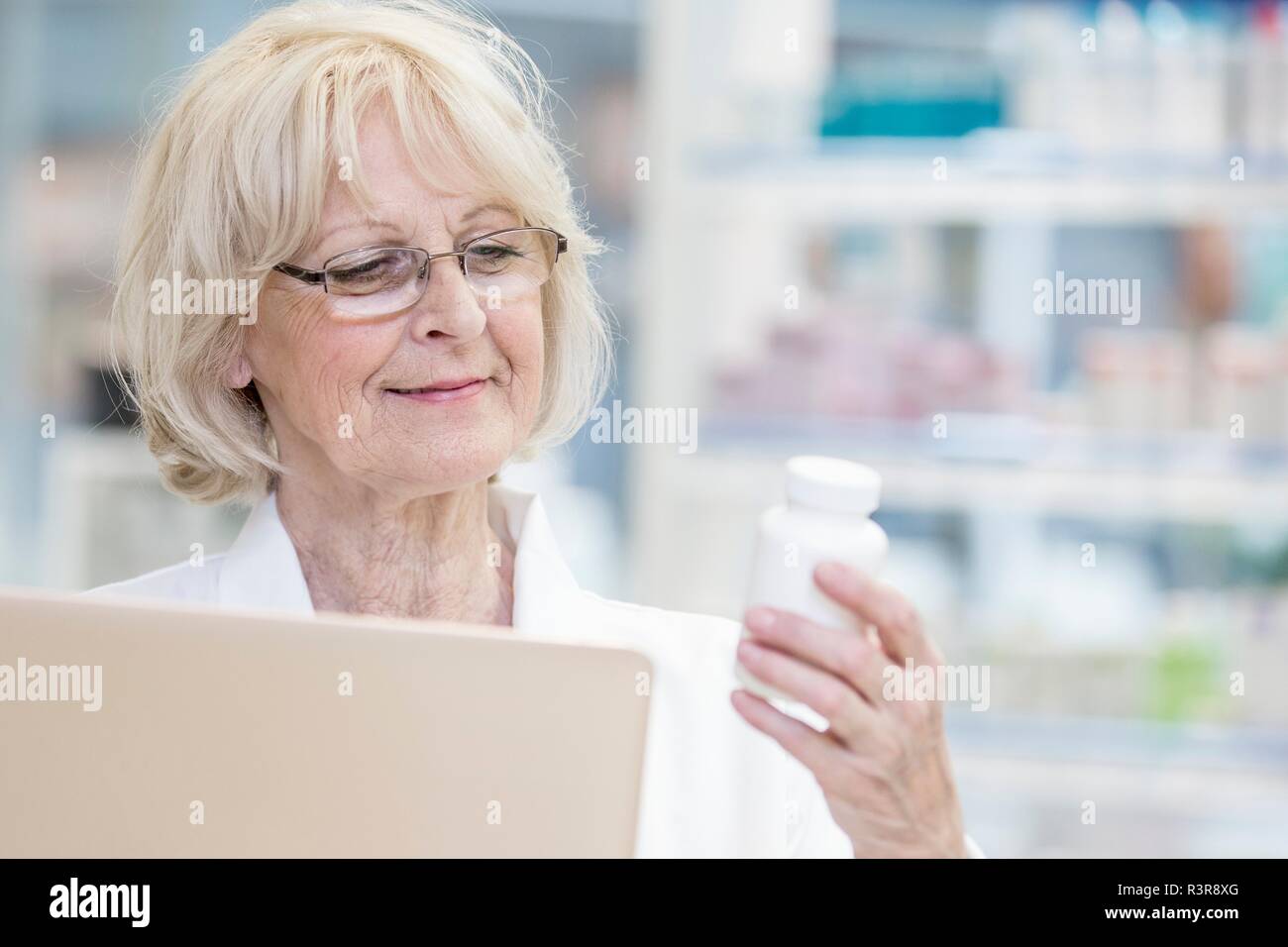 Hauts female pharmacist holding laptop et la lecture de l'étiquette sur bouteille de pilules en pharmacie. Banque D'Images