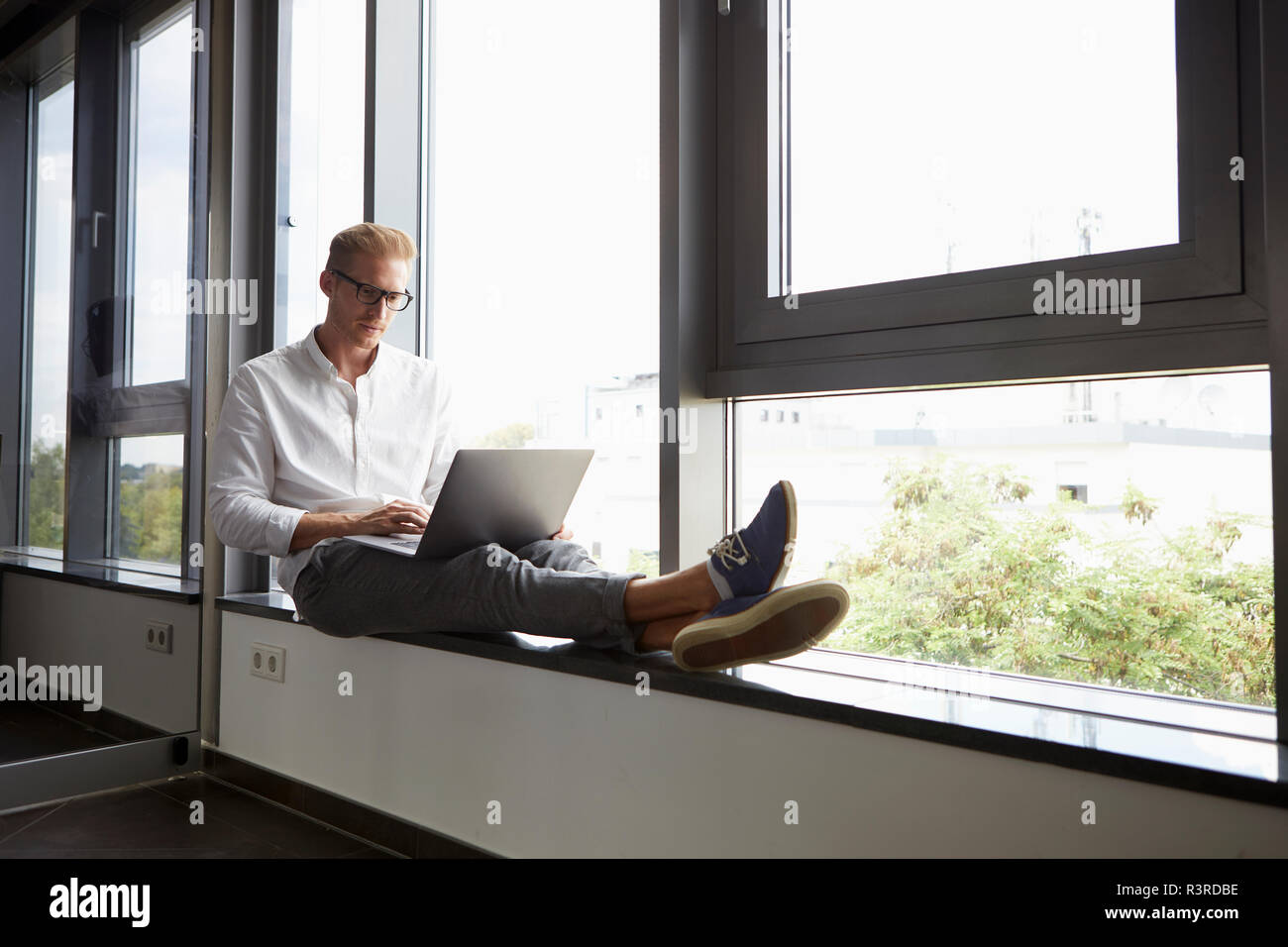 Businessman sitting on windowsill using laptop Banque D'Images