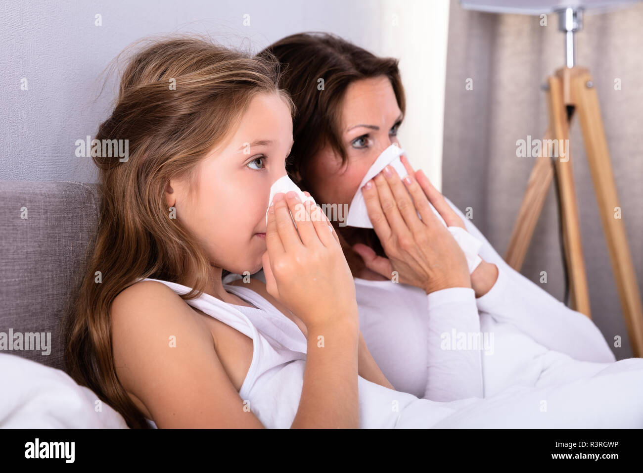 Mère et fille souffrant de soufflage froid son nez avec un mouchoir sur le lit Banque D'Images