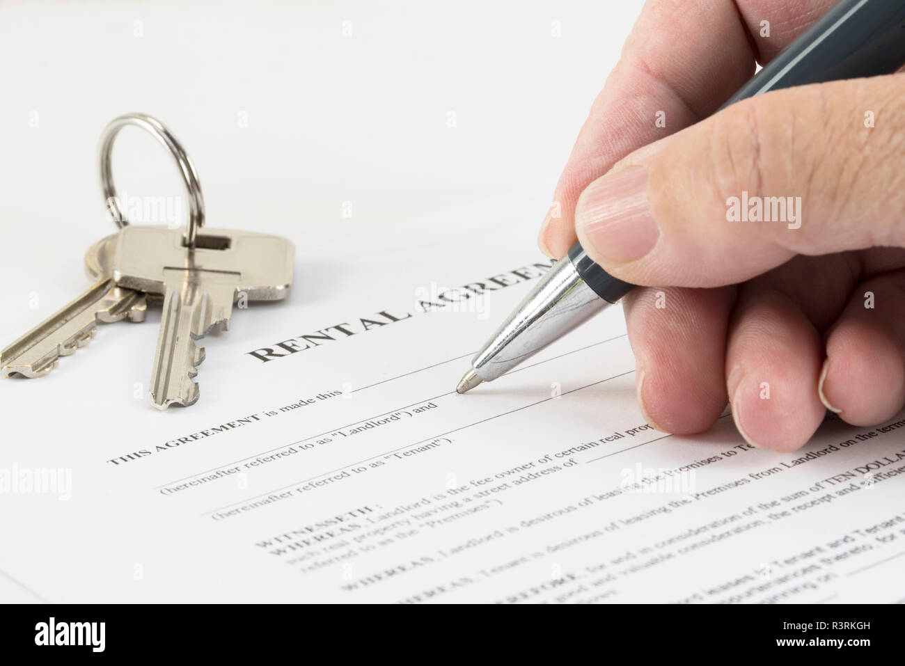 La main est écrit avec un stylo sur un contrat de location document, clés de maison dans l'arrière-plan, l'accent sélectionné, la profondeur de champ étroite Banque D'Images