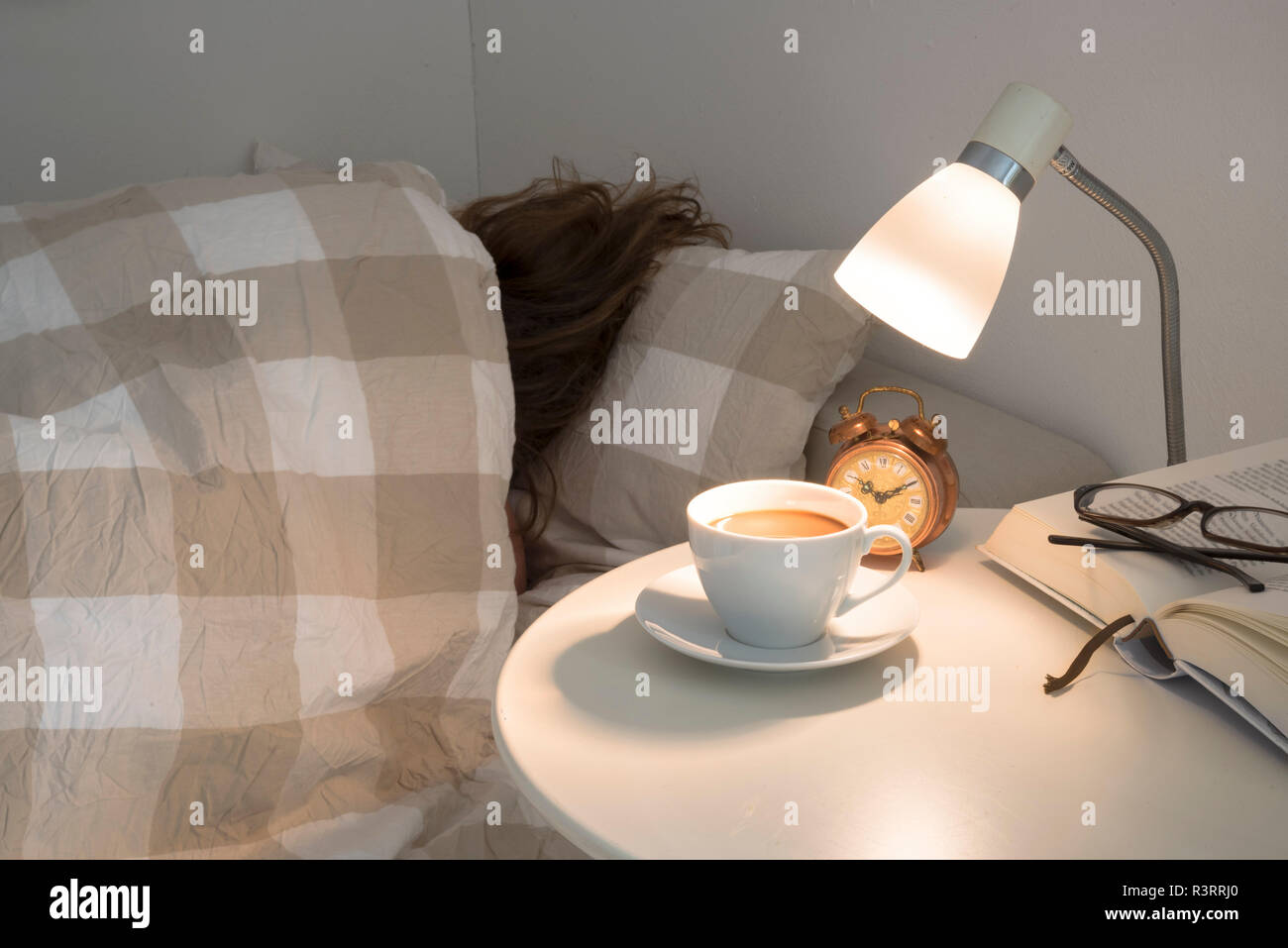 Femme dort refoulés au lit et ne veut pas se lever, la table de chevet a du café frais, un réveil et un livre, dormir sain concept, s Banque D'Images