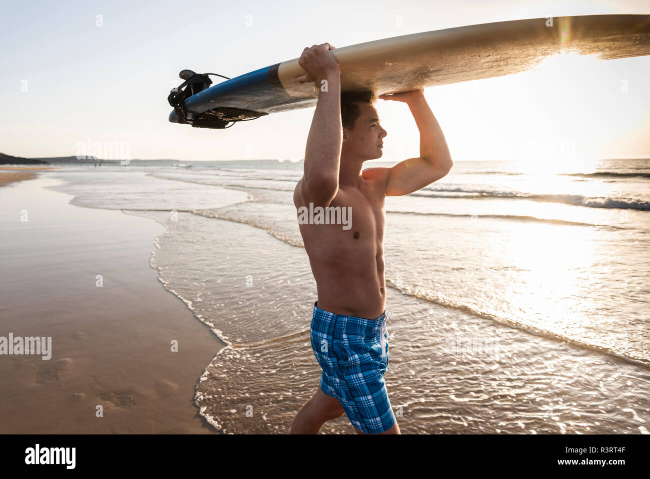 Jeune homme marchant sur la plage, sa planche de surf Banque D'Images