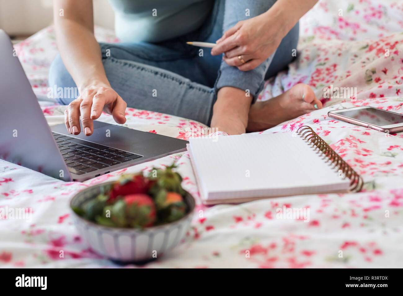 Femme assise sur le lit chez lui le travail avec ordinateur portable, vue partielle Banque D'Images