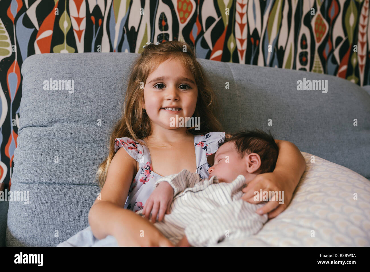 Smiling girl sitting on sofa holding newborn baby brother Banque D'Images