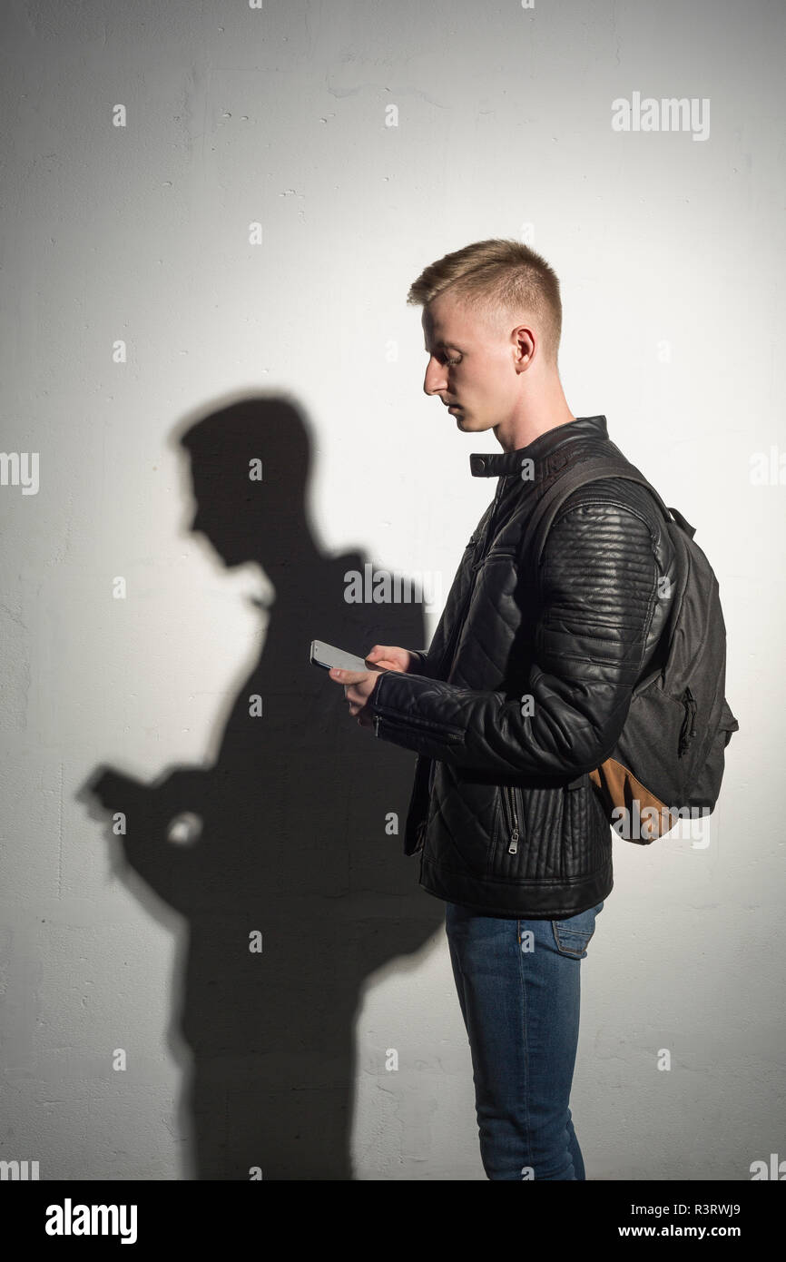 Jeune homme avec sac à dos porter veste en cuir noire looking at cell phone Banque D'Images