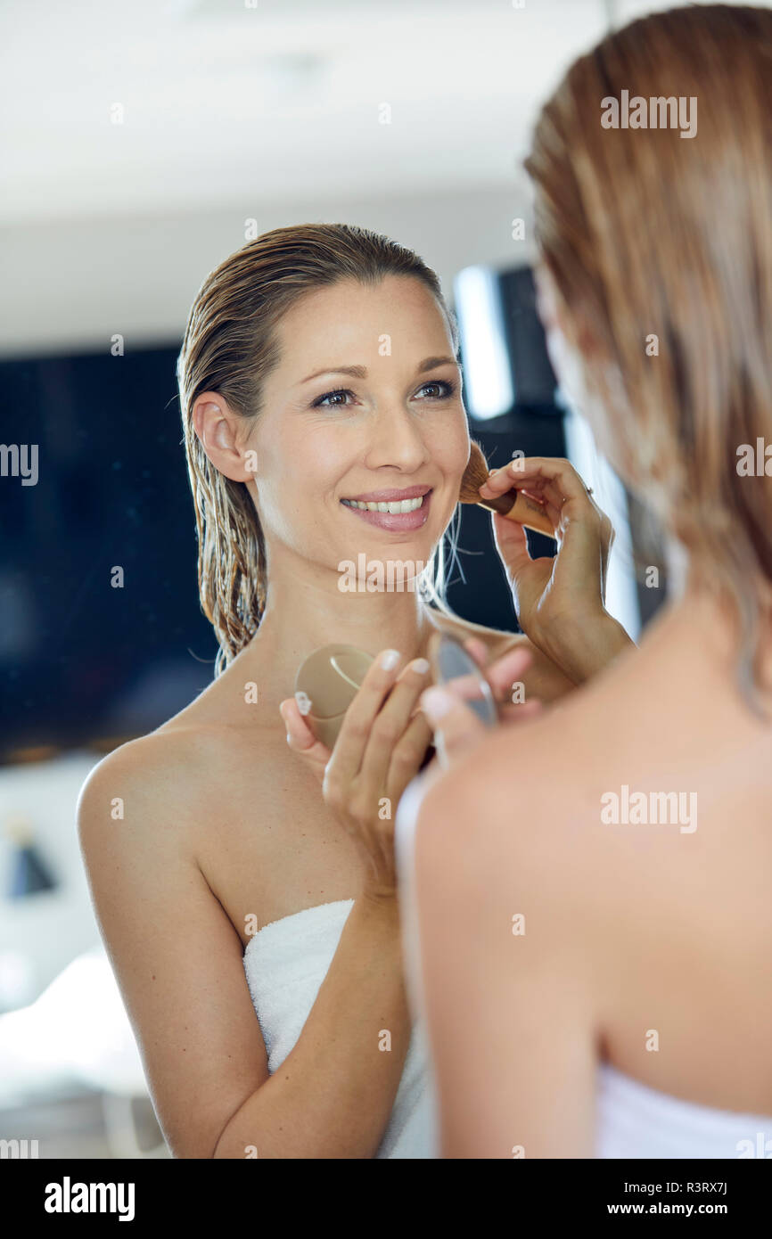 Mirror image of smiling blonde woman applying makeup Banque D'Images