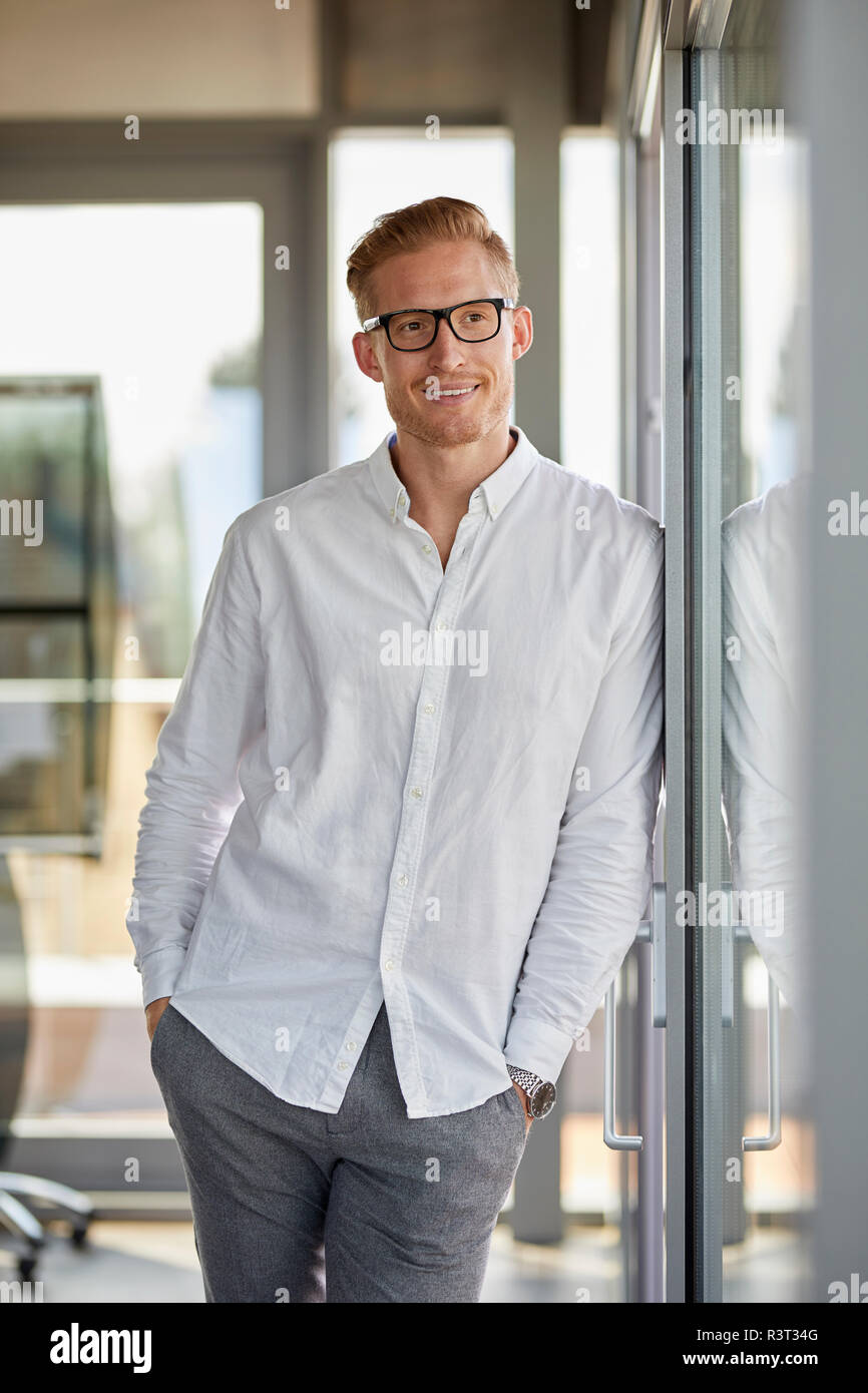 Portrait of smiling businessman in office leaning against window Banque D'Images
