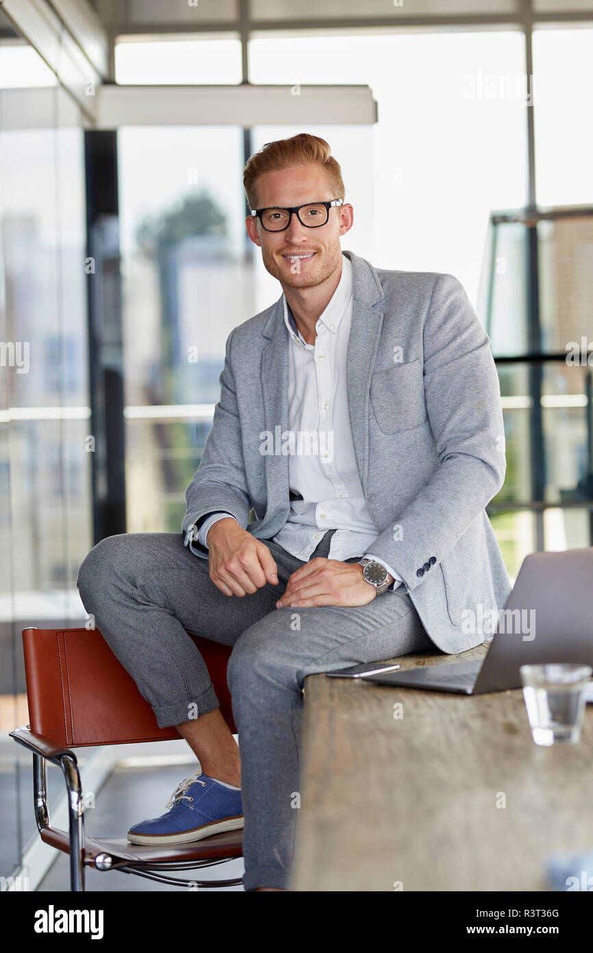 Portrait of smiling businessman with laptop sitting on desk in office Banque D'Images