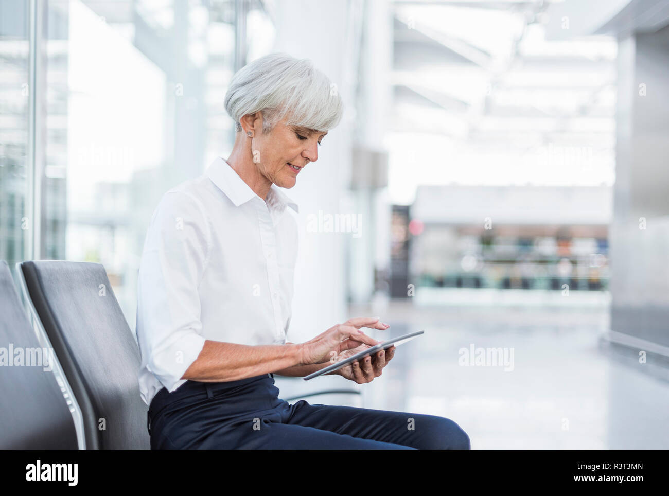 Senior businesswoman sitting in waiting area en utilisant tablet Banque D'Images