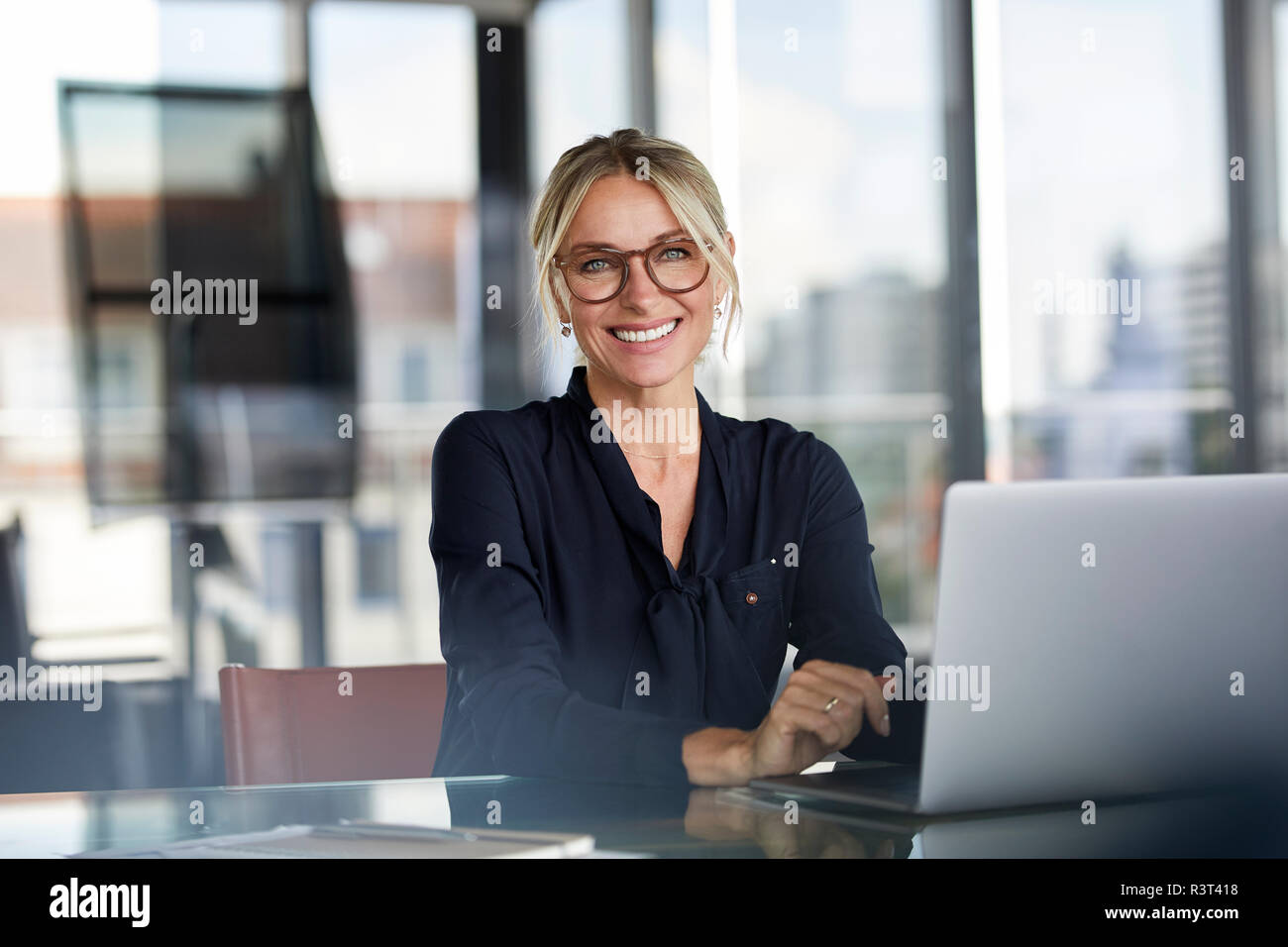 Businesswoman sitting at desk, using laptop, smiling friendly Banque D'Images