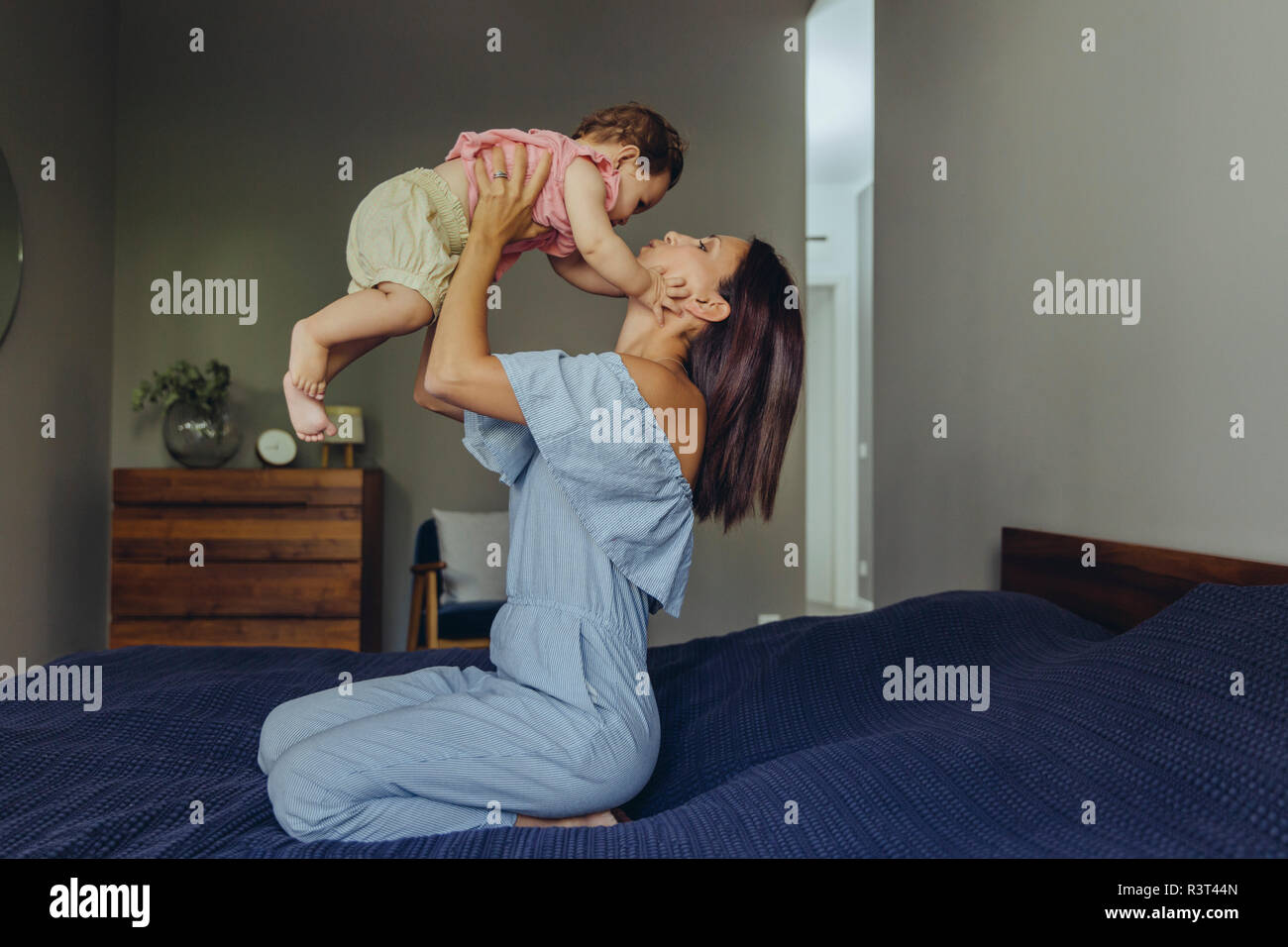 Mère soulevant son bébé girl on bed Banque D'Images