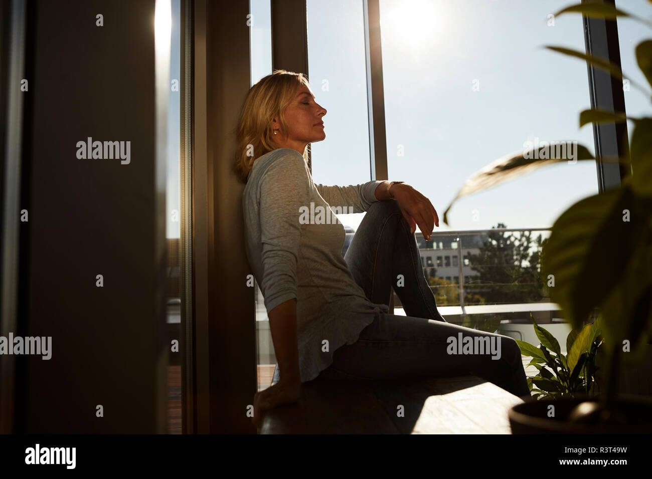 Relaxed mature femme assise dans la lumière du soleil à la maison Banque D'Images