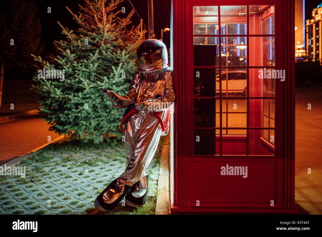 Spaceman appuyé contre une cabine téléphonique de nuit annuaire lecture Banque D'Images