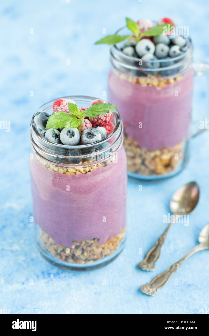 Deux verres de yogourt avec granola arachides, aronia, poudre et de noisettes hachées et les baies surgelées Banque D'Images