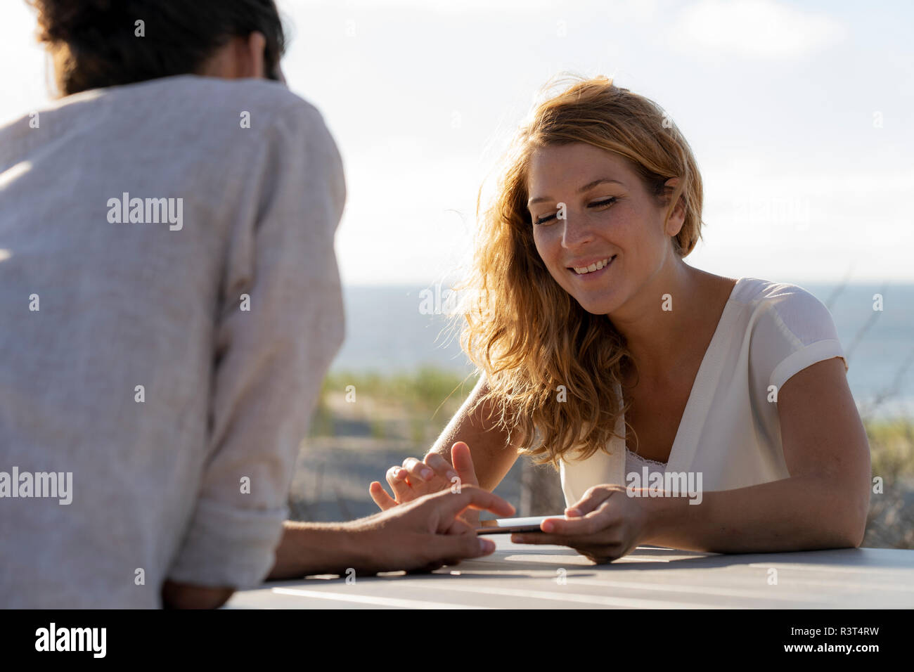 Jeune couple assis, d'un at une table à la plage Banque D'Images Jeune couple assis, d'un at une table à la plage Banque D'Images