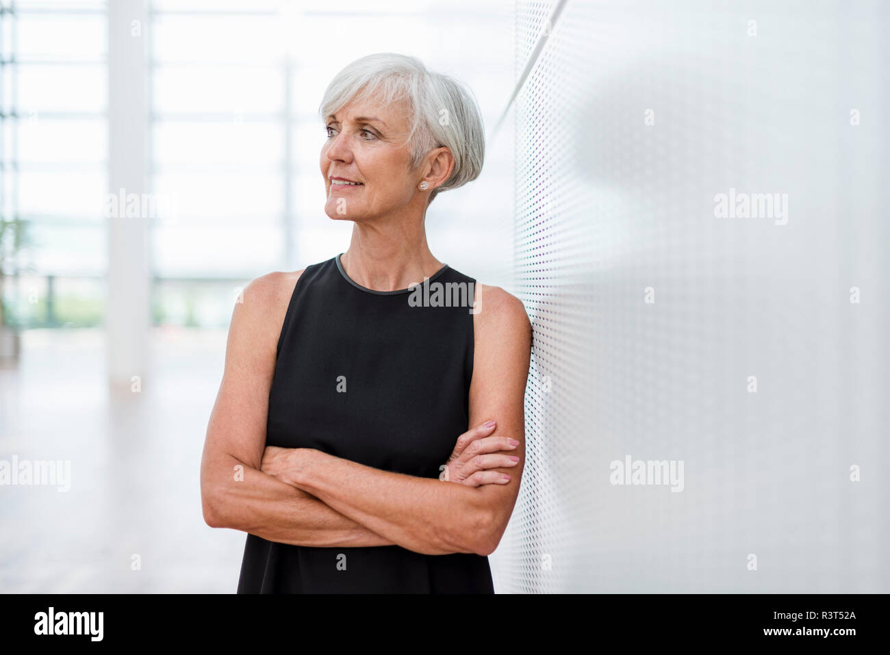 Senior woman wearing black dress appuyé contre un mur à côté Banque D'Images