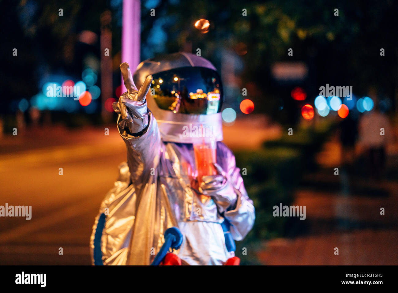 Spaceman dans la ville dans la nuit avec un verre à emporter la victoire de geste Banque D'Images