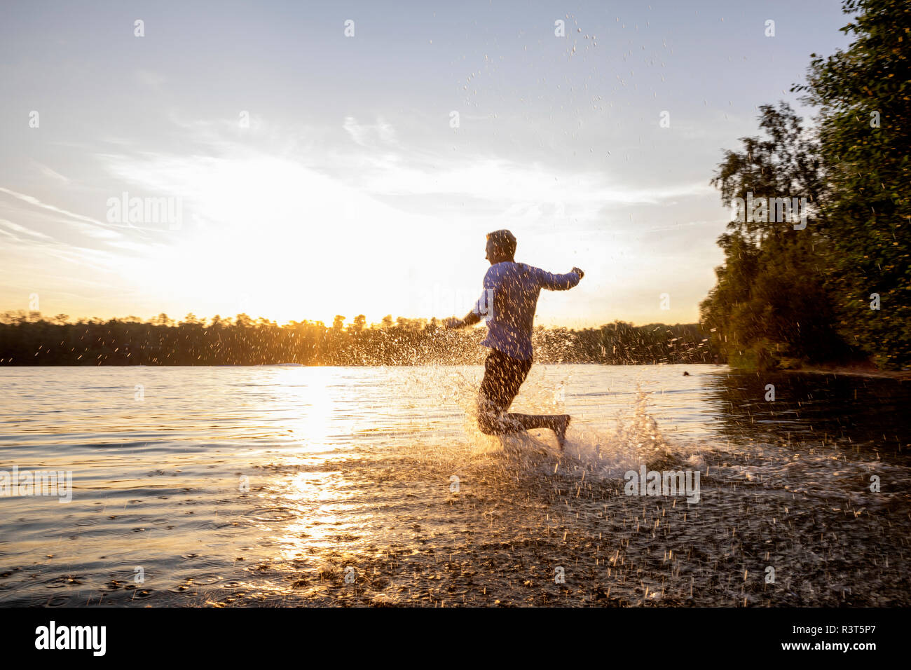 Homme qui court dans le lac par le coucher du soleil Banque D'Images