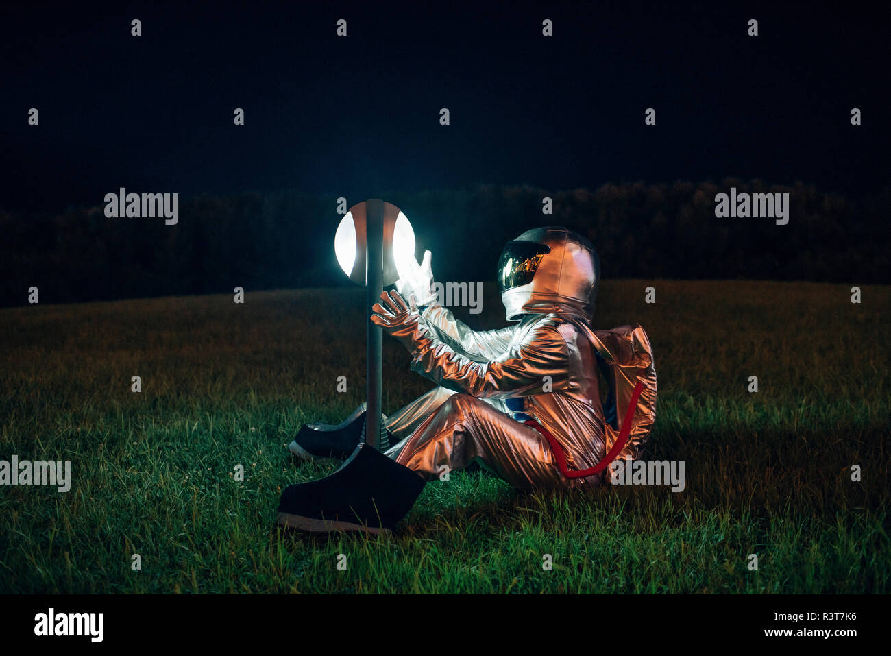 Spaceman assis sur une prairie la nuit surpris par une lampe Banque D'Images