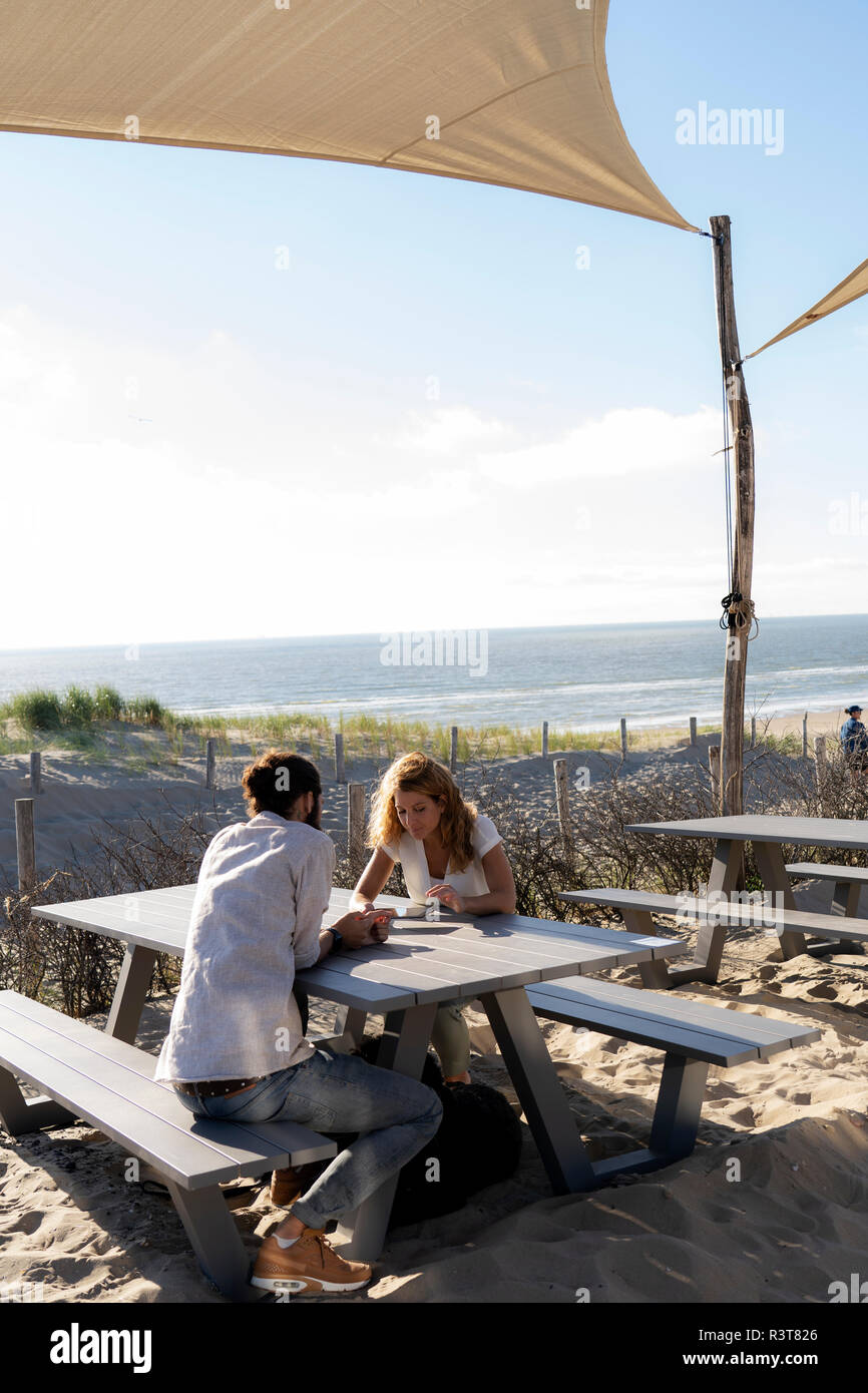 Jeune couple assis, d'un at une table à la plage Banque D'Images Jeune couple assis, d'un at une table à la plage Banque D'Images