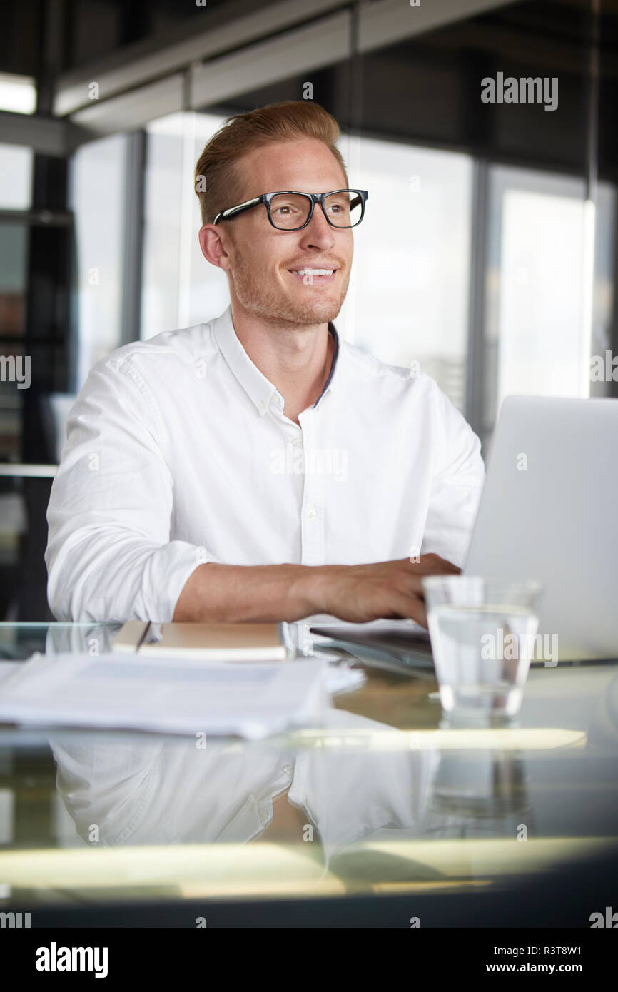 Smiling businessman with laptop on desk in office Banque D'Images