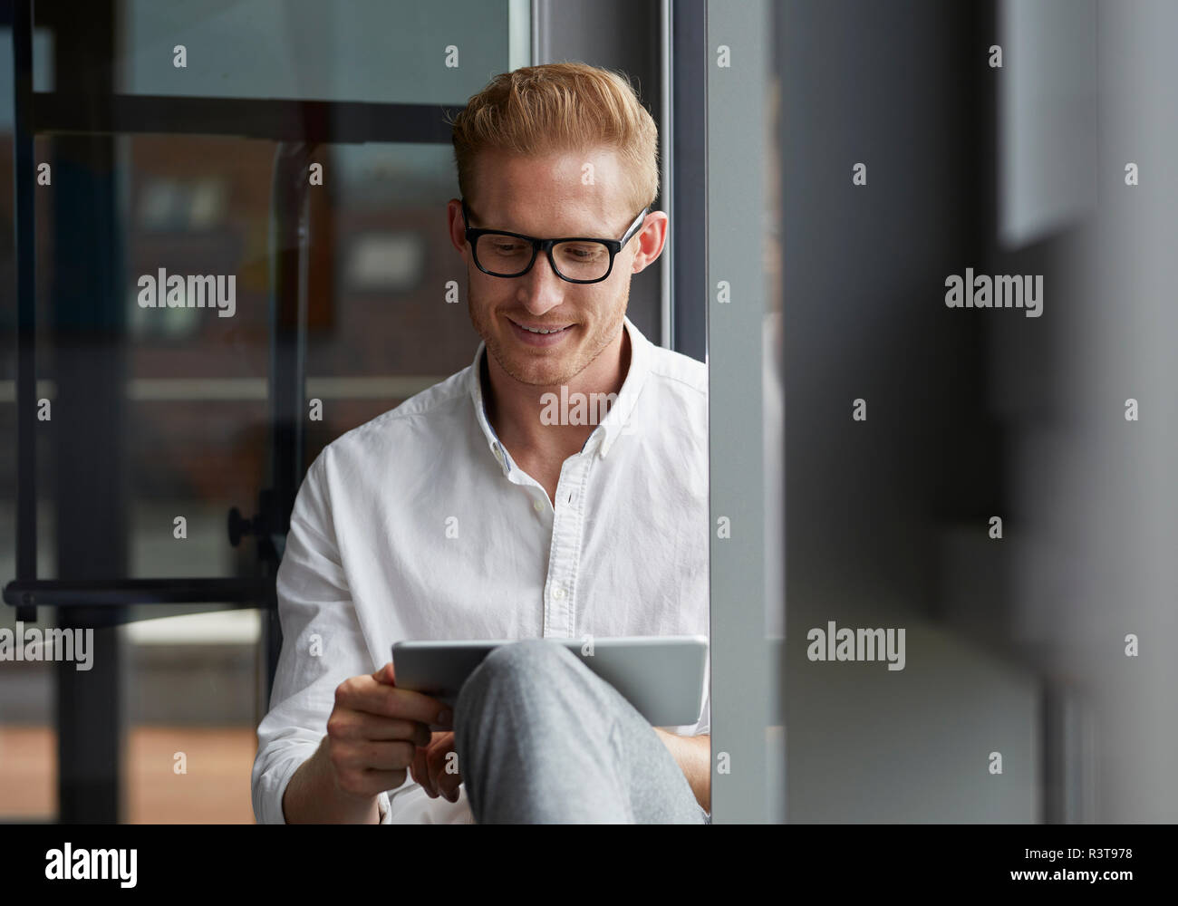 Smiling businessman sitting on windowsill using tablet Banque D'Images