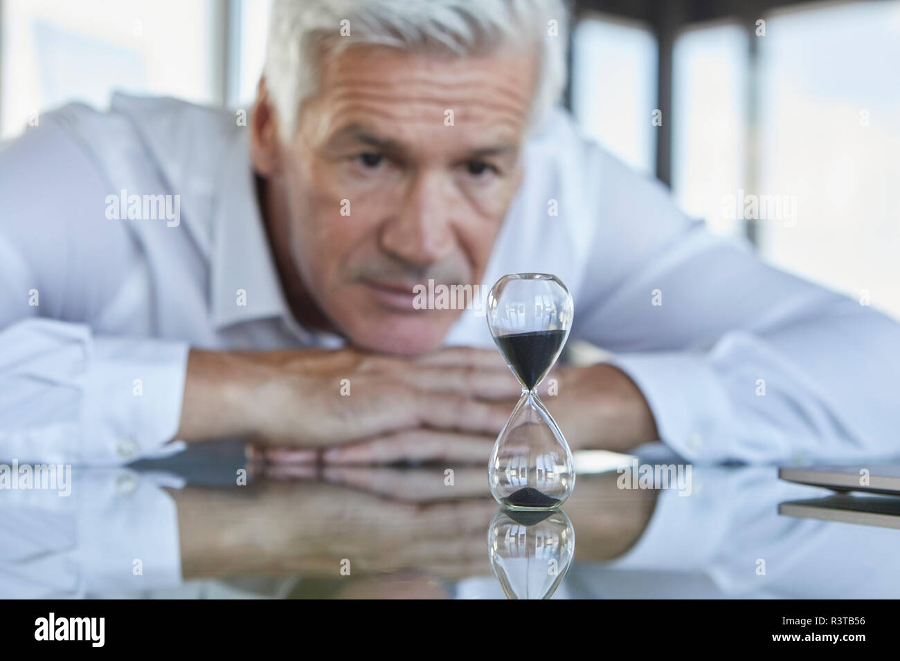 Businessman sitting at desk, regarder hourglass Banque D'Images