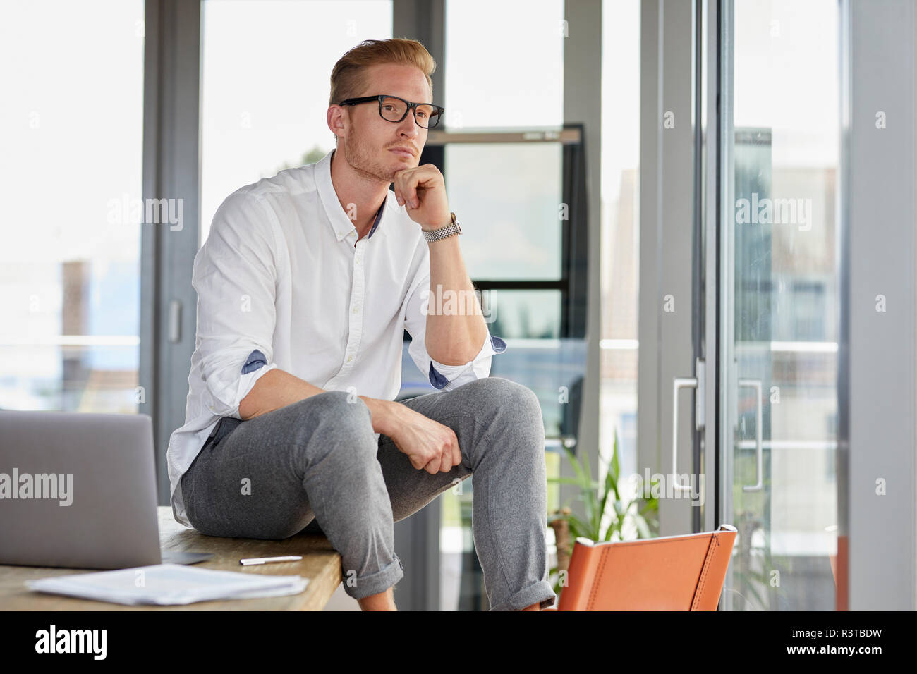 Serious businessman with laptop sitting on desk in office Banque D'Images