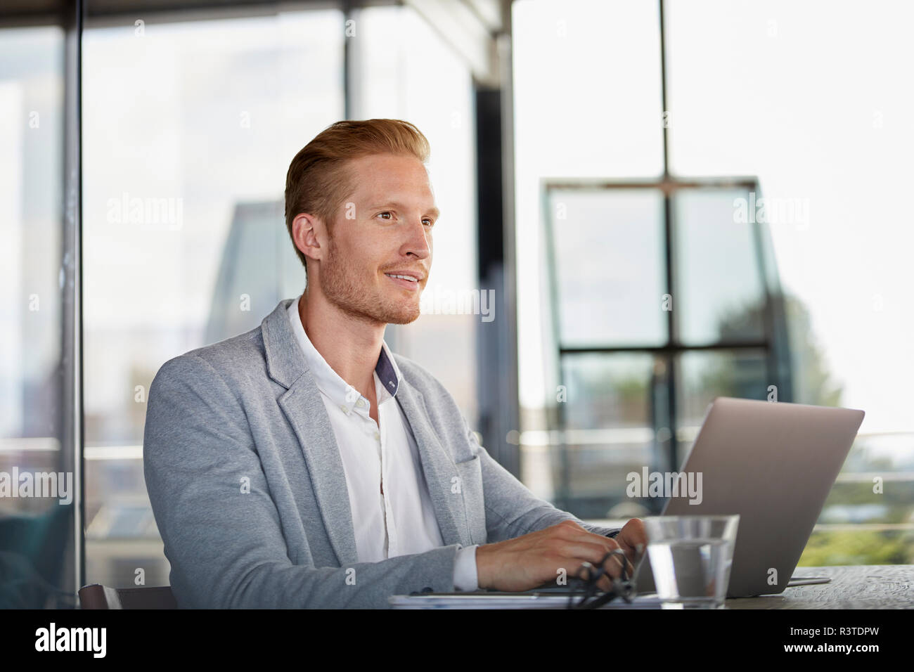 Smiling businessman with laptop on desk in office Banque D'Images