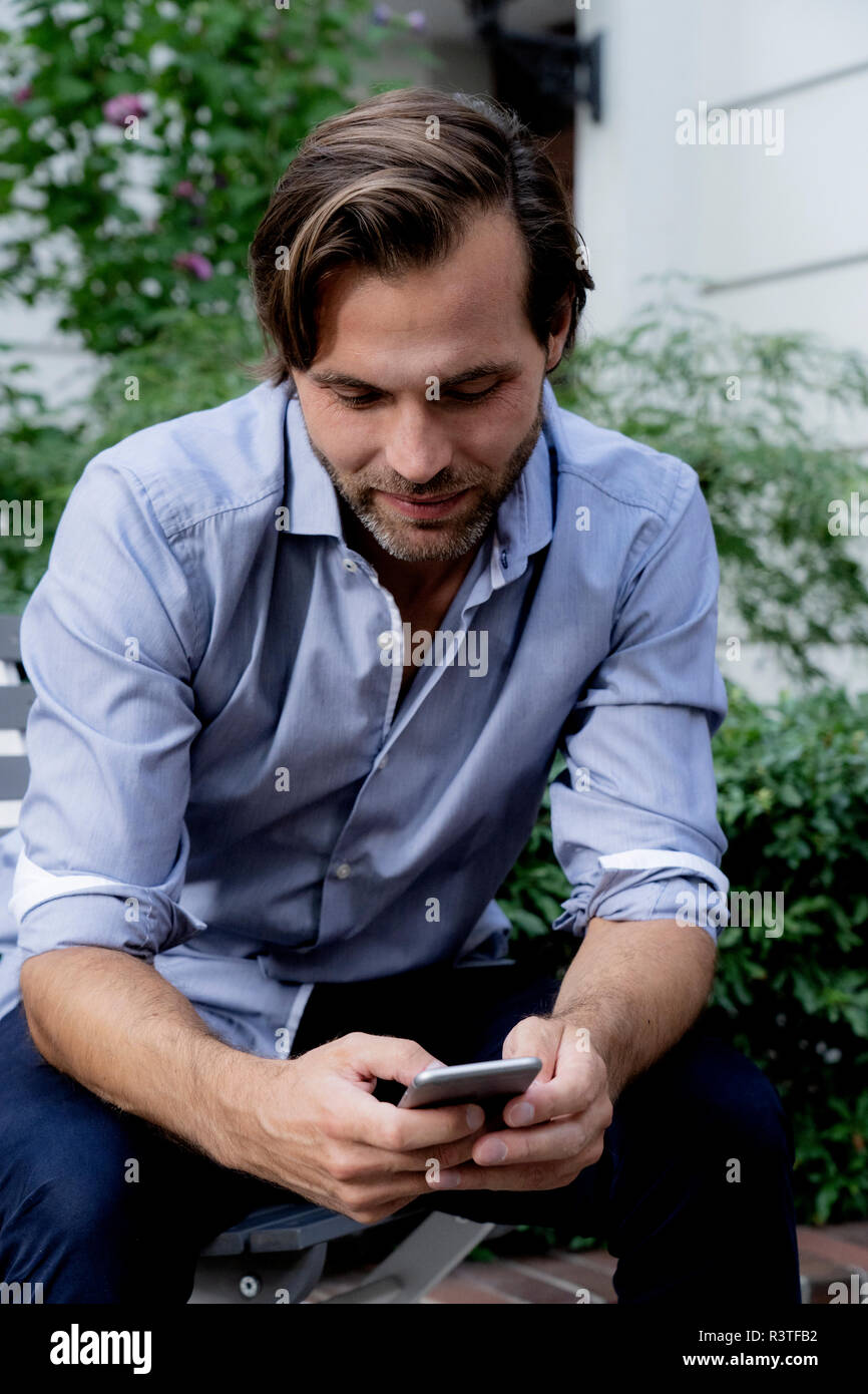 L'homme assis sur une chaise de jardin using cell phone Banque D'Images L'homme assis sur une chaise de jardin using cell phone Banque D'Images