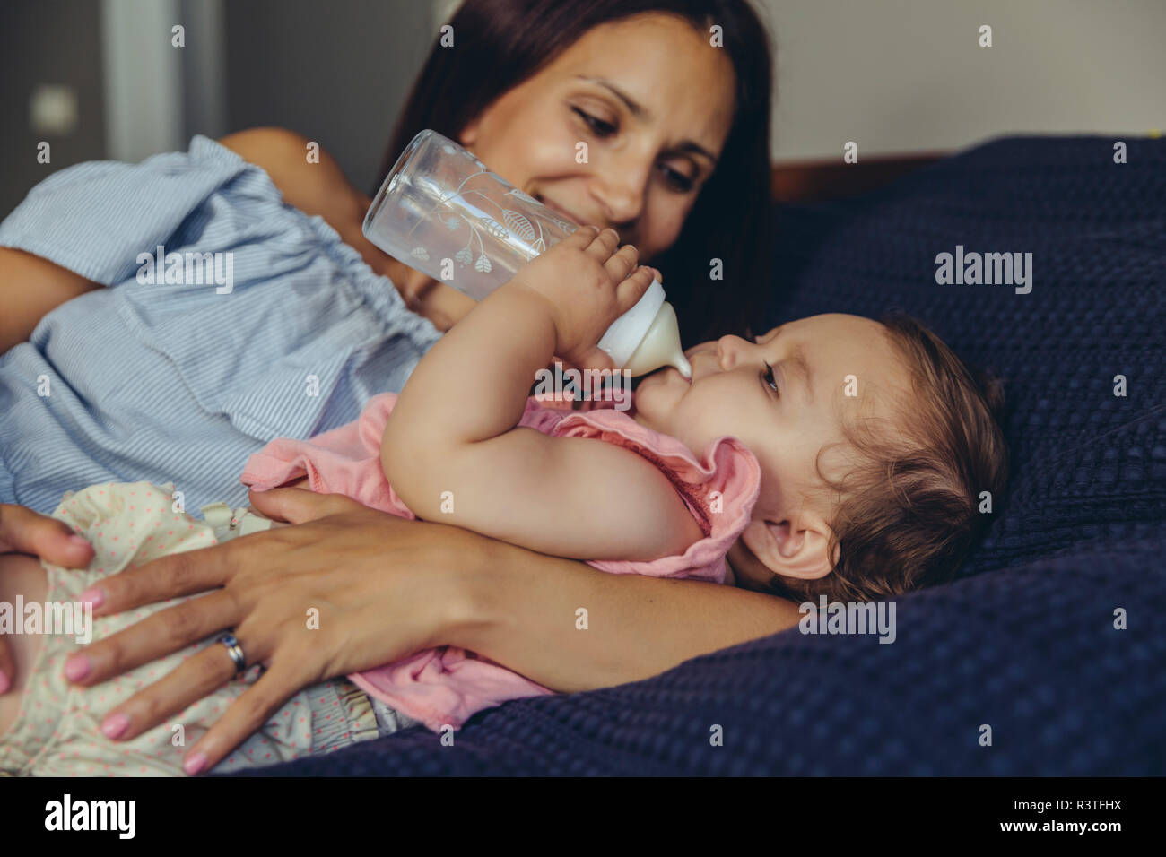 Mère regardant son bébé boire du lait d'une bouteille on bed Banque D'Images