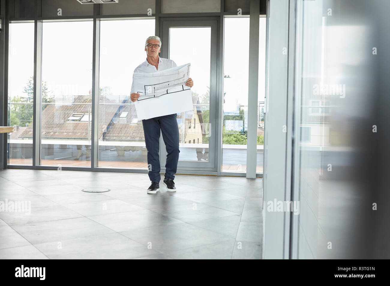 Successful businessman standing in office, holding construction plan Banque D'Images