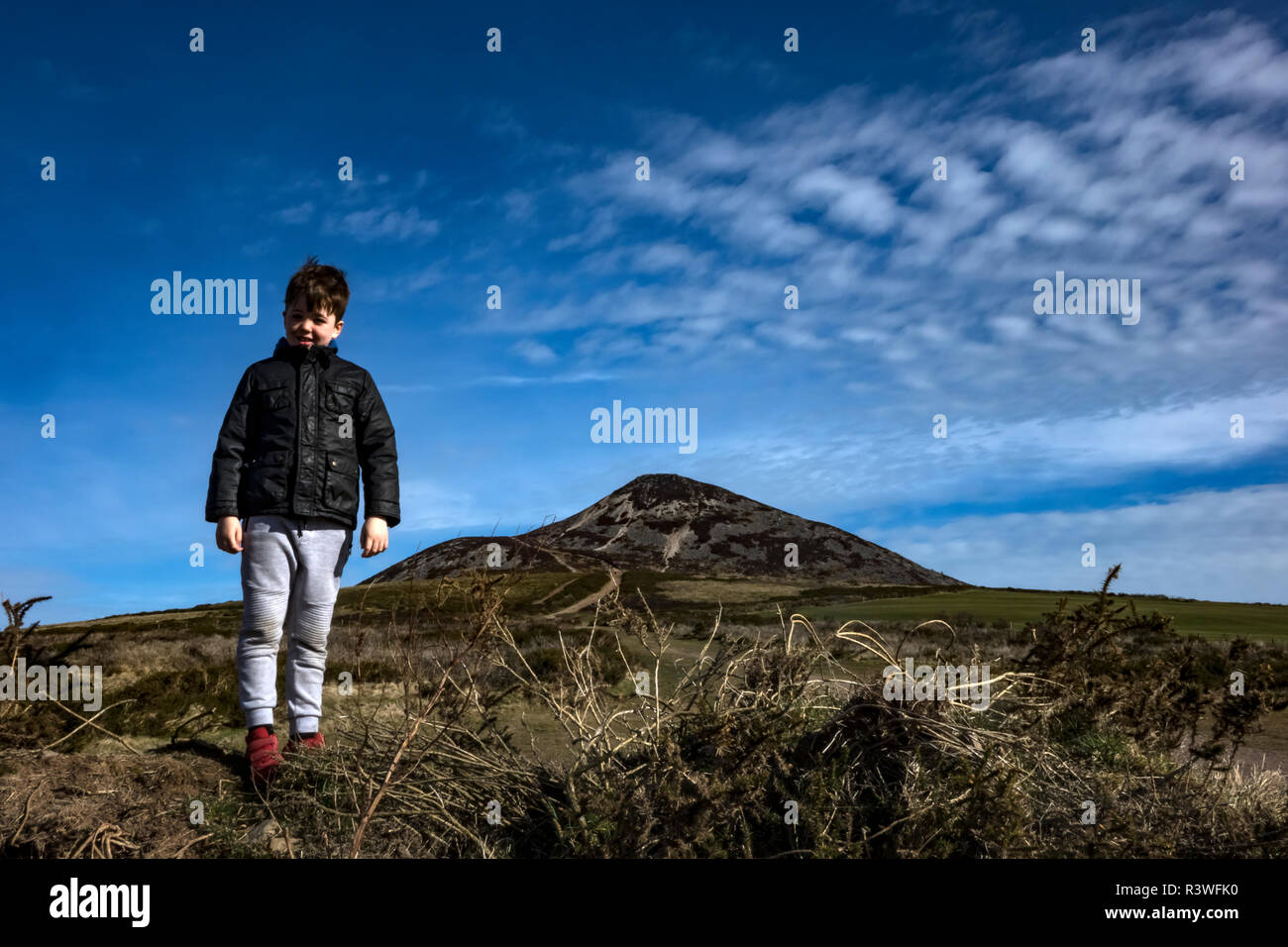 Jeune garçon sous un ciel bleu avec des nuages blancs sur un jour lumineux en face de la montagne Sugarloaf dans le comté de Wicklow, Irlande de l'ouest bordant le norther Banque D'Images