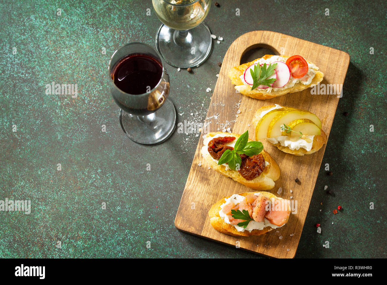 Antipasti italiens des en-cas pour le vin. Variété Brushetta avec fromage doux, de poire, de radis, de saumon et tomates séchées servi sur une planche en bois rustique sur Banque D'Images