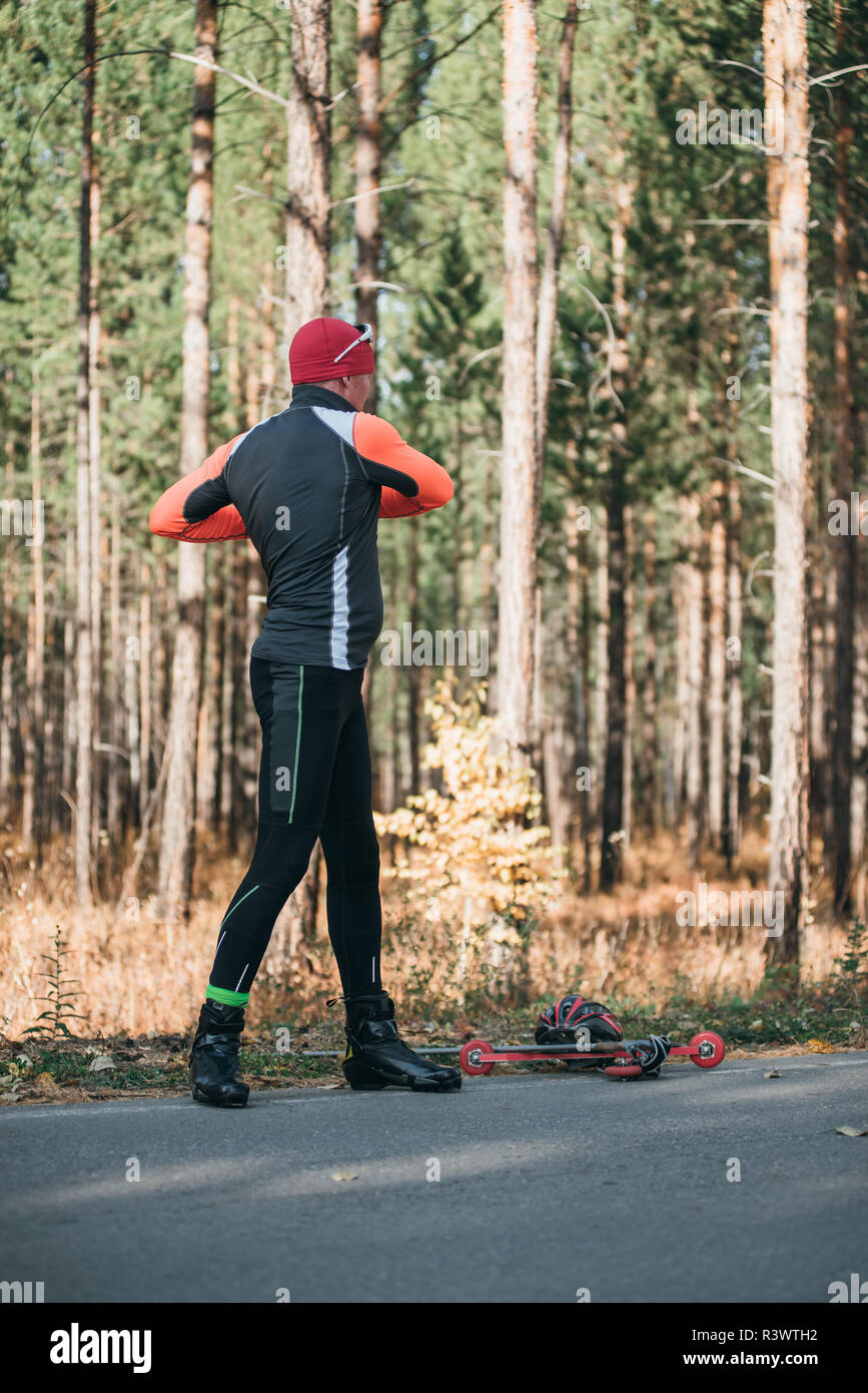 Un athlète, à la formation de patins à roulettes. Le Biathlon tour sur les skis à roulettes avec des bâtons de ski, dans le casque. Entraînement d'automne. Roller sport. Débarrasser l'homme adultes Banque D'Images