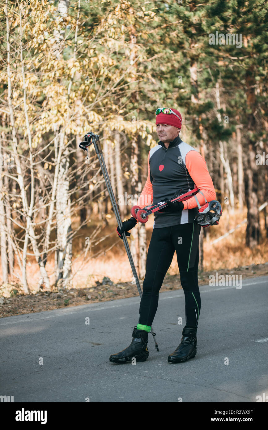 Un athlète, à la formation de patins à roulettes. Le Biathlon tour sur les skis à roulettes avec des bâtons de ski, dans le casque. Entraînement d'automne. Roller sport. Débarrasser l'homme adultes Banque D'Images