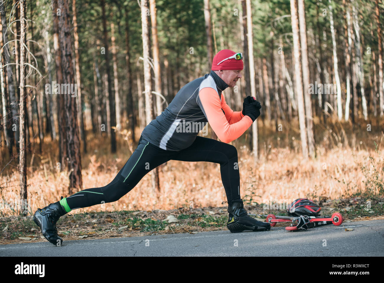 Un athlète, à la formation de patins à roulettes. Le Biathlon tour sur les skis à roulettes avec des bâtons de ski, dans le casque. Entraînement d'automne. Roller sport. Débarrasser l'homme adultes Banque D'Images