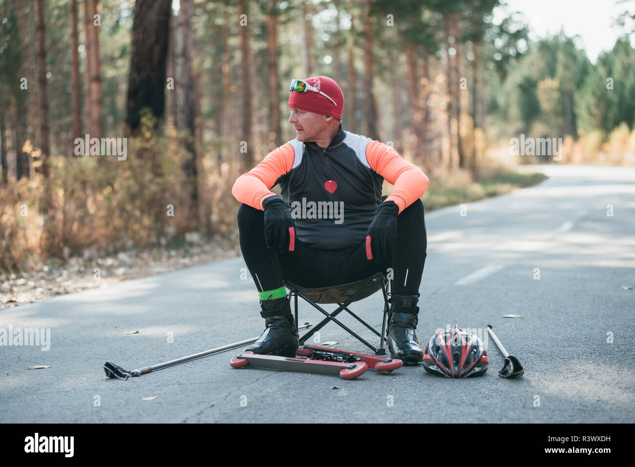 Un athlète, à la formation de patins à roulettes. Le Biathlon tour sur les skis à roulettes avec des bâtons de ski, dans le casque. Entraînement d'automne. Roller sport. Débarrasser l'homme adultes Banque D'Images