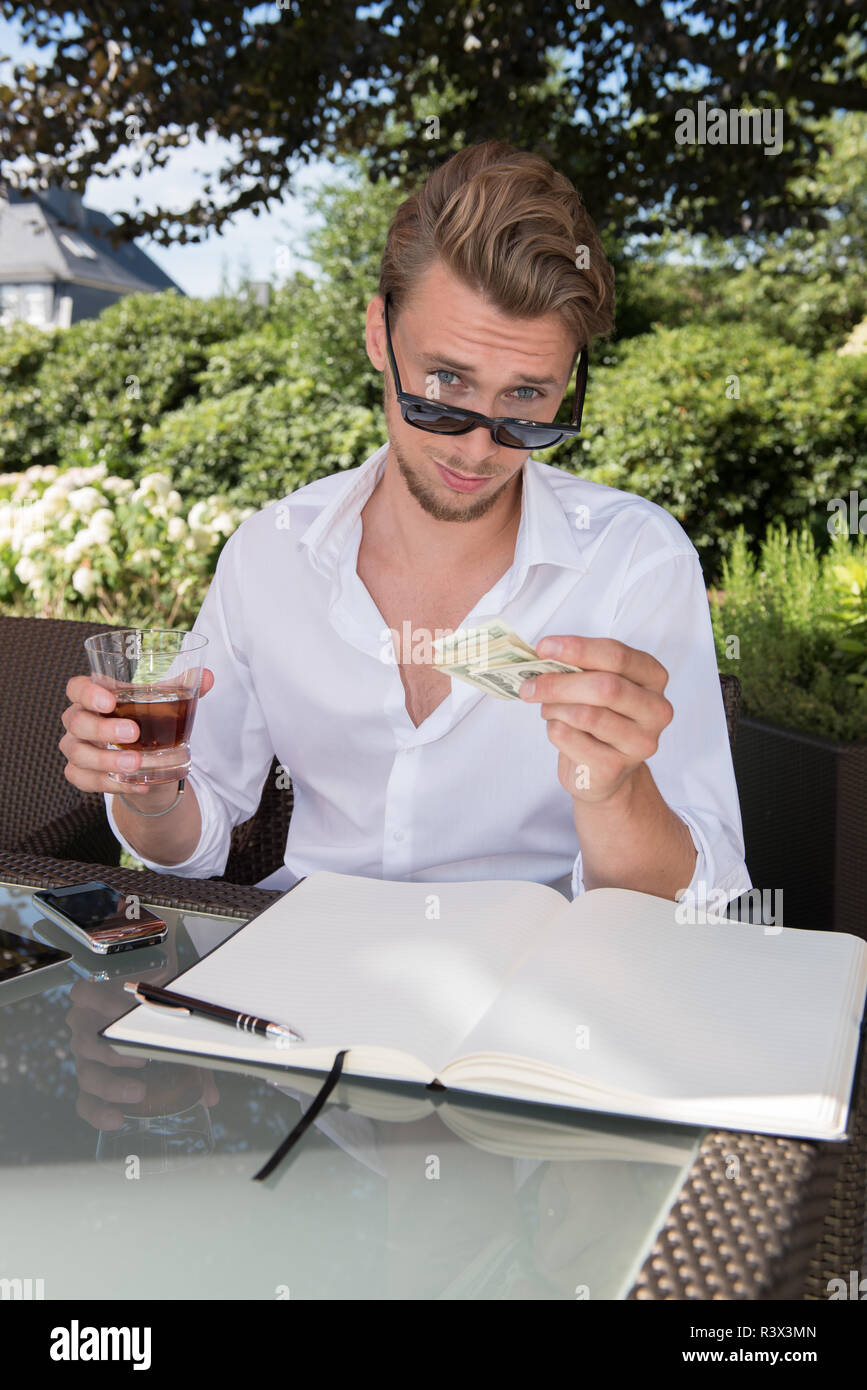 Jeune homme d'affaires compte de dollars dans le jardin et prendre un verre Banque D'Images