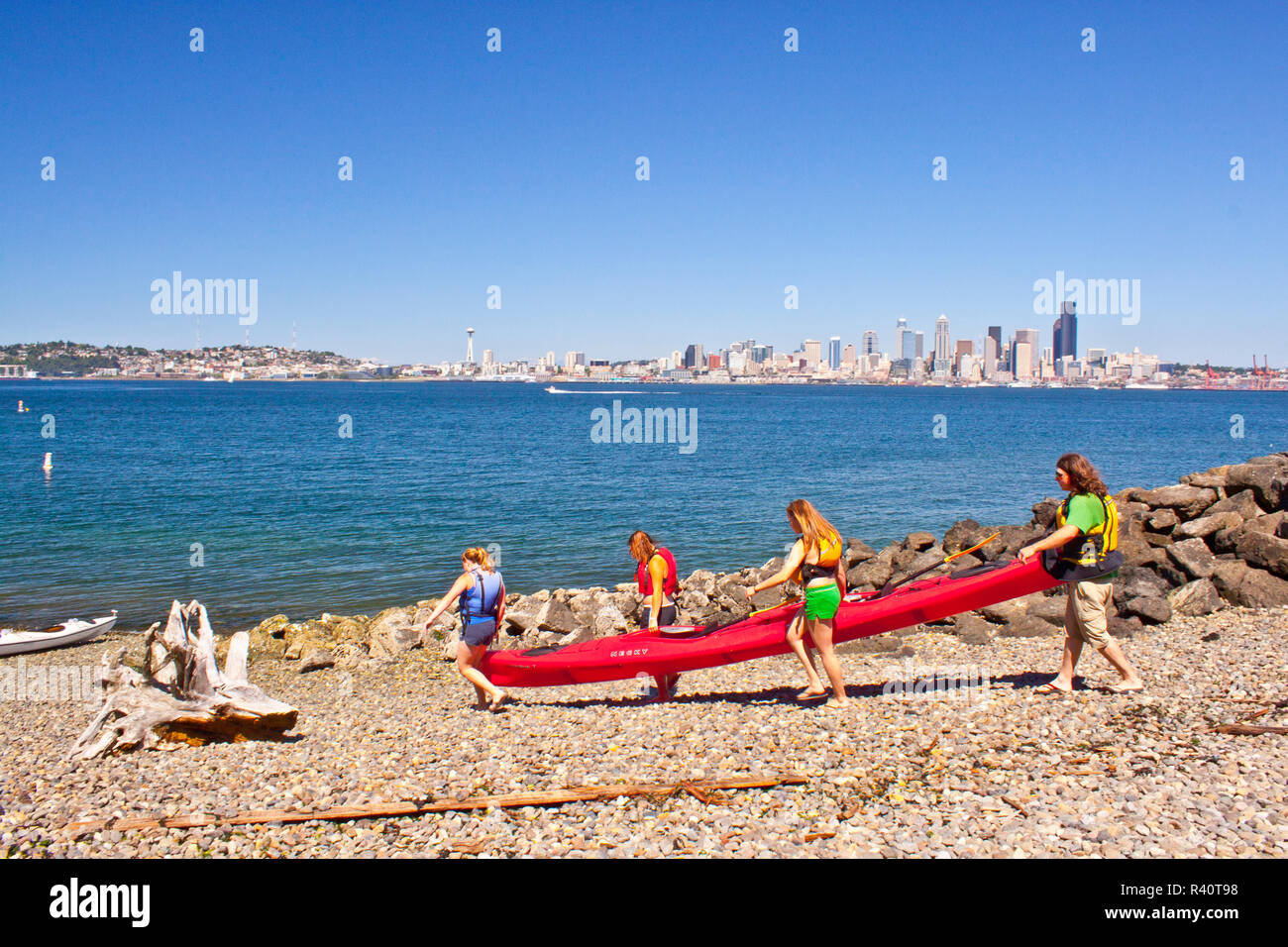USA, l'État de Washington, Seattle. Les gens portent un kayak de mer pour deux personnes sur une plage de West Seattle, dans le Puget Sound du centre-ville de Seattle. Banque D'Images