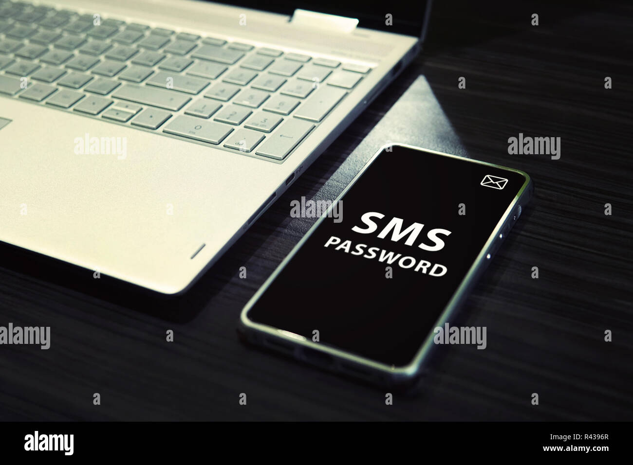 Table avec open laptop noir et blanc d'un smartphone avec des mots écrits mot de passe par SMS sur son afficheur. Idée d'unir le travail d'ordinateur et mobile via mot de passe par sms entrant. L'un code temporel. Banque D'Images